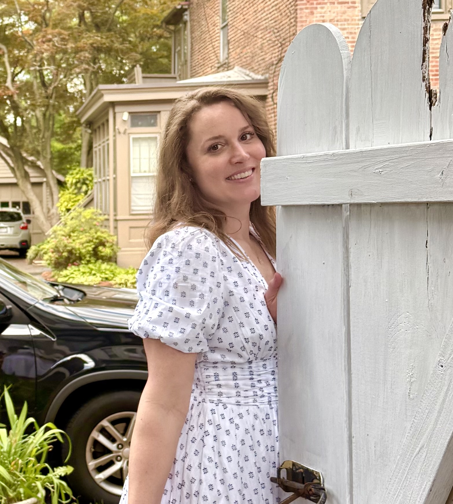 girl in white dress smiling and standing next to gate